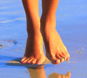 Woman' s feet on water's edge at a sandy beach